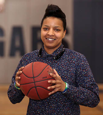 Female basketball star smiling and holding a basketball in the Columbus State gymnasium.