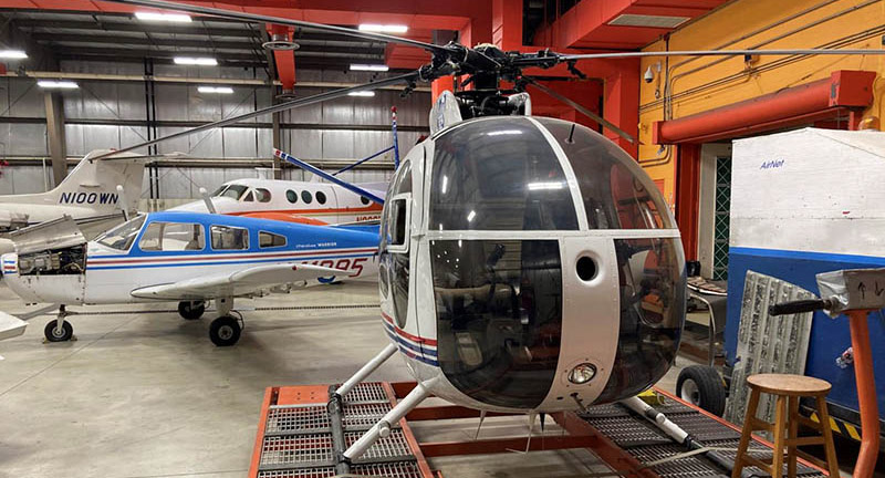 Hughes 369HS Helicopter in foreground with various single and twin engine planes in background.