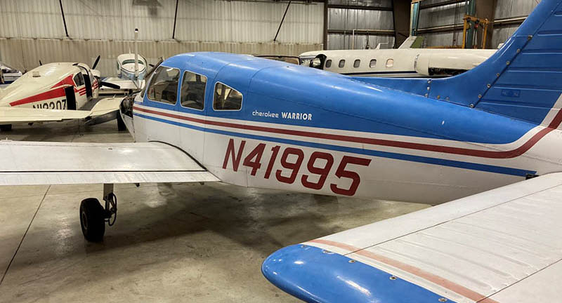 Single engine airplanes in hanger. Piper PA28 151 in foreground.