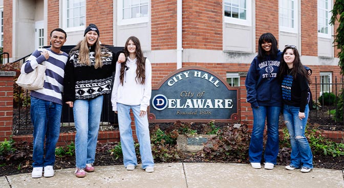 Students posing in front of a sign downtown Delaware Ohio.