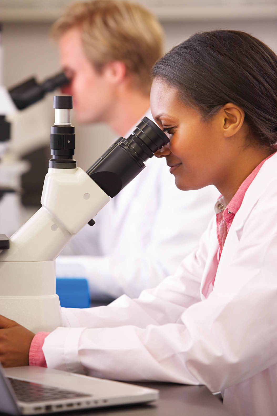 Male And Female Scientists Using Microscopes In Laboratory